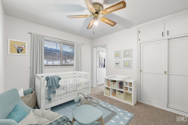 bedroom featuring a crib, a ceiling fan, a closet, and light colored carpet