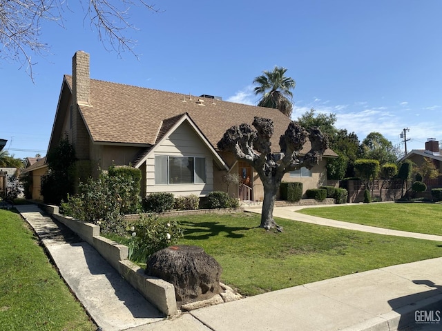 view of front facade with a chimney, roof with shingles, and a front yard