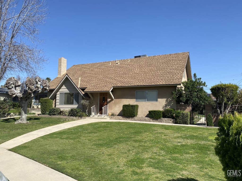 view of front of property with a front yard, roof with shingles, a chimney, and stucco siding