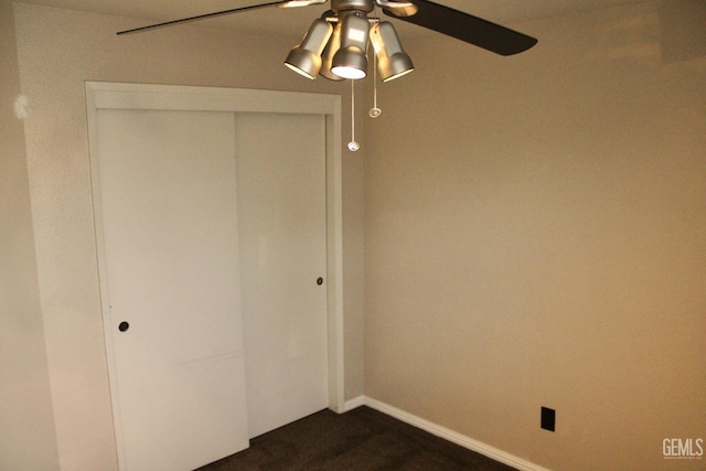 unfurnished bedroom with a closet, ceiling fan, dark colored carpet, and baseboards