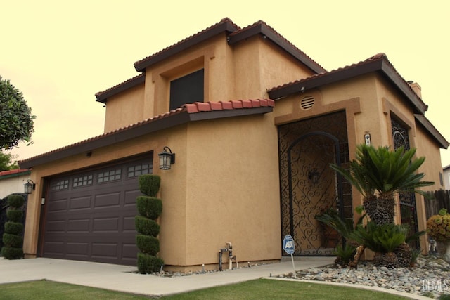 view of front facade with a garage, stucco siding, a tile roof, and driveway