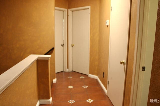 hallway with tile patterned floors, an upstairs landing, and baseboards