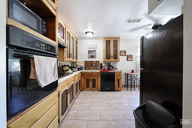 kitchen featuring backsplash, tile counters, light tile patterned floors, and black appliances