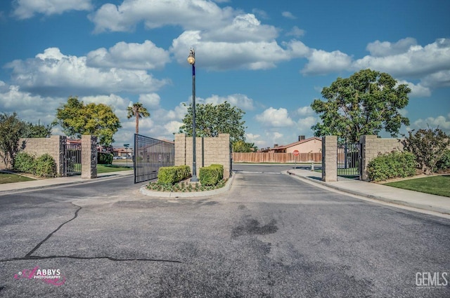 view of asphalt street with a gate, sidewalks, curbs, and a gated entry