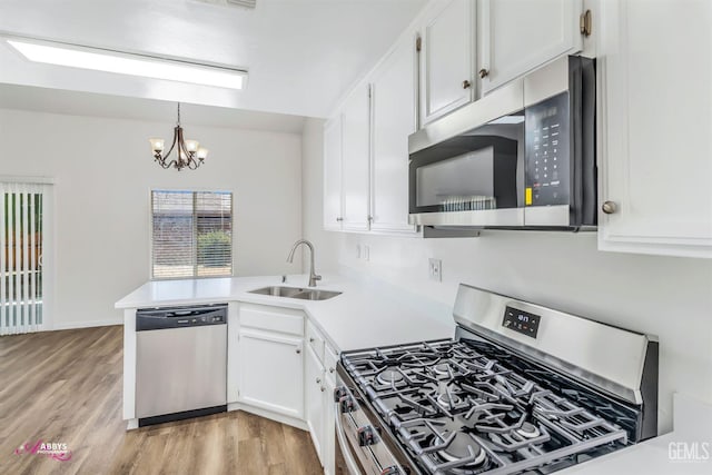 kitchen with appliances with stainless steel finishes, a peninsula, white cabinetry, and a chandelier