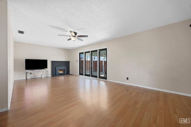 unfurnished living room with a brick fireplace, a textured ceiling, hardwood / wood-style flooring, and ceiling fan