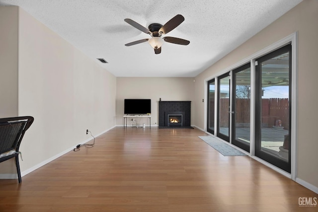 unfurnished living room featuring ceiling fan, hardwood / wood-style floors, a fireplace, and a textured ceiling