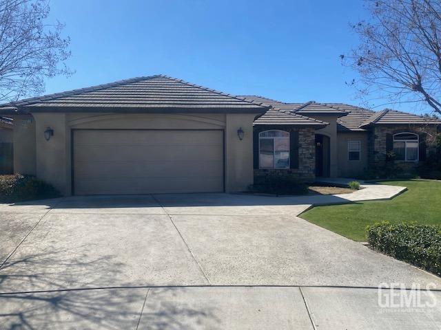 single story home featuring a garage, driveway, a tiled roof, a front lawn, and stucco siding