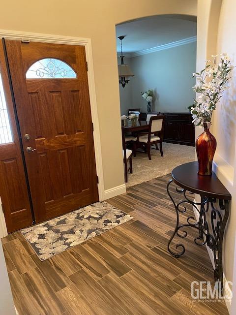 entryway with ornamental molding, wood finished floors, and baseboards