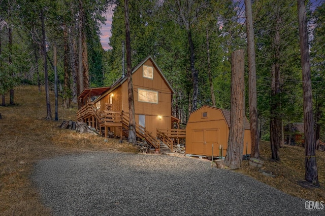 chalet / cabin featuring a wooded view, stairway, a storage shed, and an outdoor structure