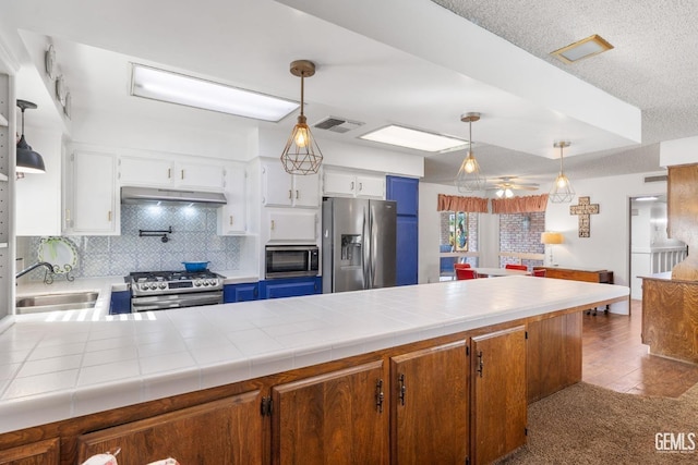 kitchen with tile counters, sink, stainless steel appliances, range hood, and white cabinets