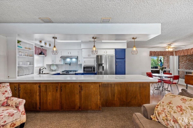 kitchen with kitchen peninsula, appliances with stainless steel finishes, decorative light fixtures, and white cabinetry