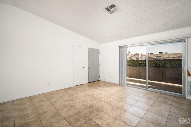 empty room featuring a textured ceiling, vaulted ceiling, and light tile patterned floors