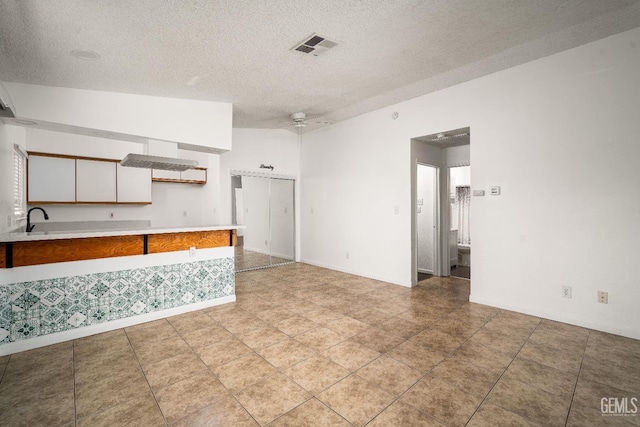 kitchen featuring a textured ceiling, vaulted ceiling, white cabinets, ceiling fan, and sink