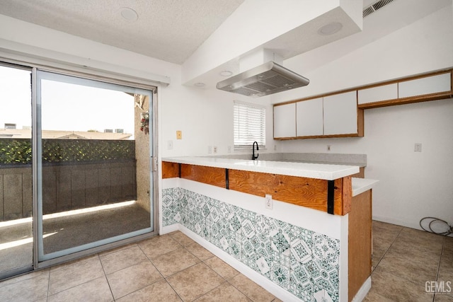 kitchen with white cabinets, a textured ceiling, vaulted ceiling, light tile patterned flooring, and kitchen peninsula