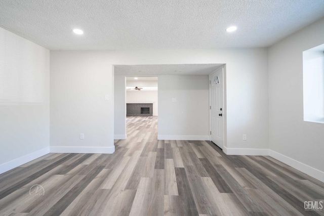 unfurnished room with a textured ceiling, wood finished floors, baseboards, and recessed lighting