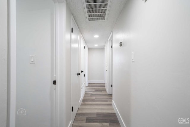 hall with visible vents, baseboards, a textured ceiling, recessed lighting, and wood finished floors