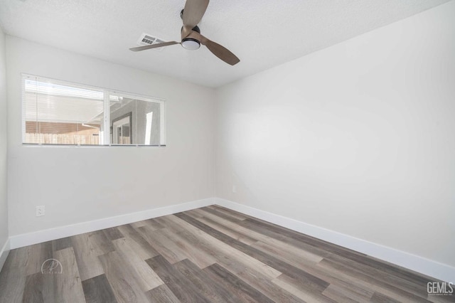 empty room featuring a textured ceiling, a ceiling fan, visible vents, wood finished floors, and baseboards