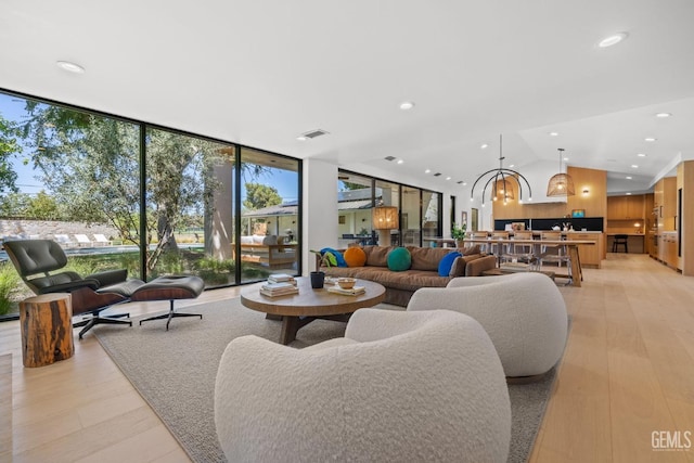 living room with light wood-type flooring, vaulted ceiling, visible vents, recessed lighting, and expansive windows