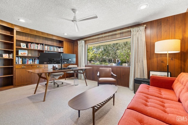 office area featuring wood walls, a textured ceiling, ceiling fan, and light colored carpet