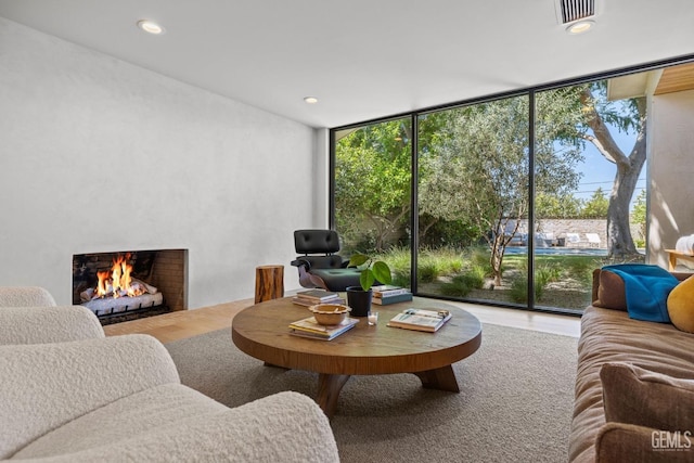 living area featuring wood finished floors, floor to ceiling windows, a fireplace with flush hearth, visible vents, and recessed lighting