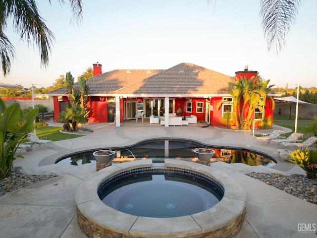 pool at dusk featuring a patio and an in ground hot tub