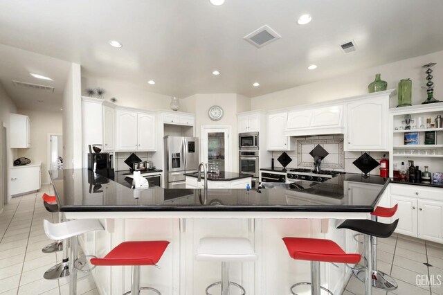 kitchen featuring white cabinets, stainless steel appliances, a kitchen breakfast bar, backsplash, and light tile patterned flooring