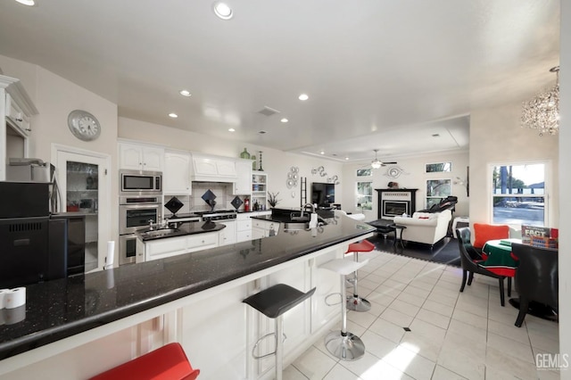 kitchen featuring tasteful backsplash, a kitchen bar, light tile patterned flooring, stainless steel appliances, and white cabinets