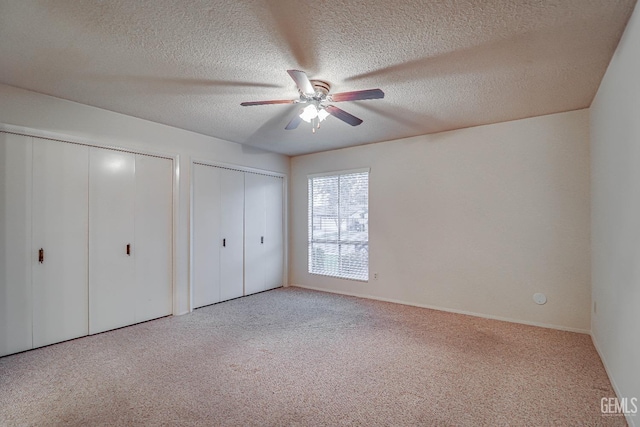 unfurnished bedroom with light carpet, a textured ceiling, two closets, and ceiling fan