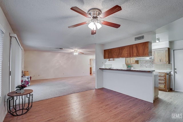 kitchen featuring kitchen peninsula, backsplash, a textured ceiling, light hardwood / wood-style floors, and range hood