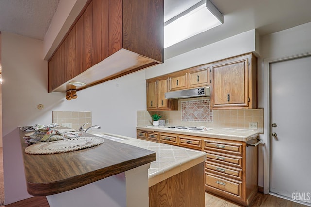 kitchen featuring sink, tasteful backsplash, white gas stovetop, light hardwood / wood-style flooring, and tile countertops