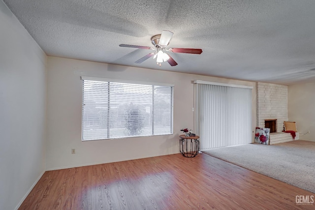 interior space with a textured ceiling, ceiling fan, light wood-type flooring, and a fireplace