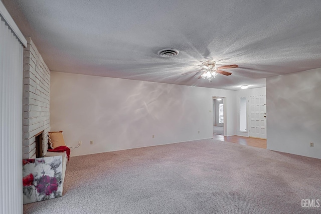 unfurnished living room featuring a textured ceiling, ceiling fan, light colored carpet, and a fireplace