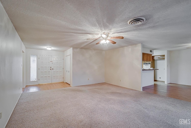 unfurnished living room featuring light carpet, ceiling fan, and a textured ceiling