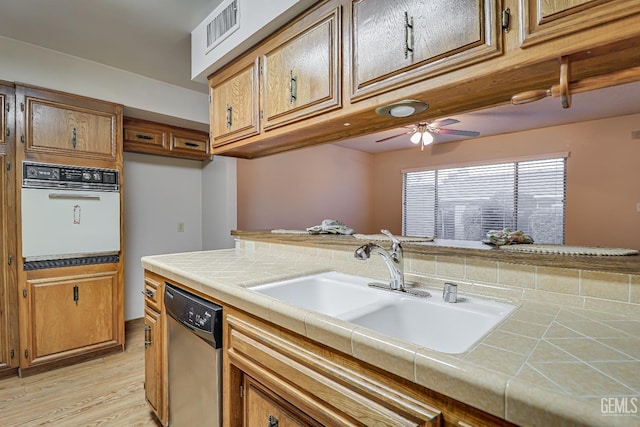 kitchen with stainless steel dishwasher, ceiling fan, sink, tile countertops, and oven