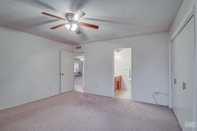 unfurnished bedroom with light carpet, a textured ceiling, ensuite bathroom, and ceiling fan