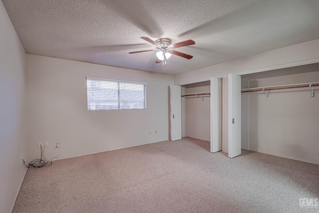 unfurnished bedroom featuring carpet flooring, a textured ceiling, ceiling fan, and multiple closets