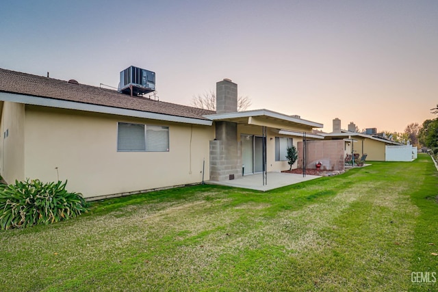 back house at dusk featuring a patio, a lawn, and central air condition unit