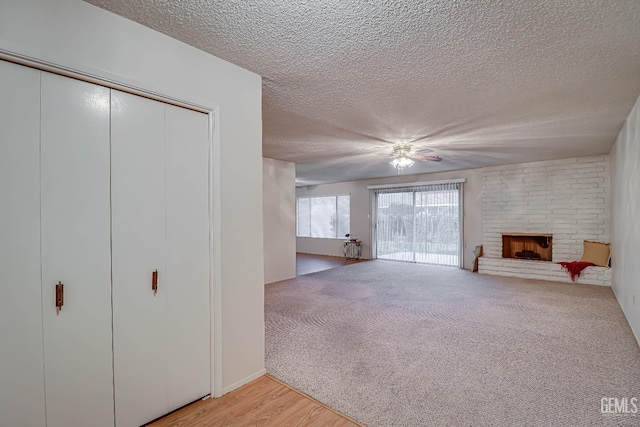 unfurnished living room with a fireplace, a textured ceiling, light colored carpet, and ceiling fan