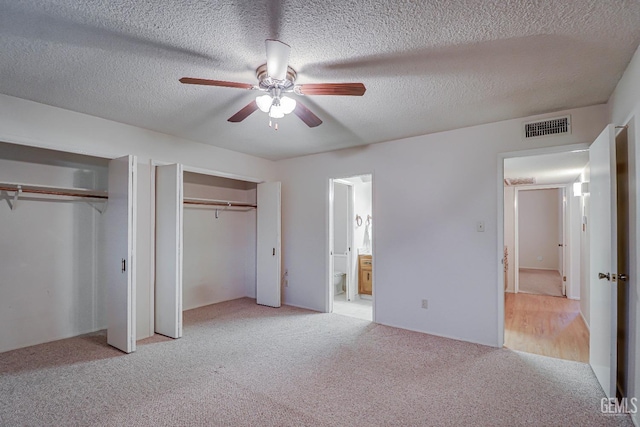 unfurnished bedroom with ceiling fan, ensuite bathroom, light colored carpet, a textured ceiling, and two closets