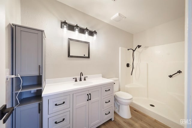 bathroom with a shower, toilet, wood finished floors, and vanity