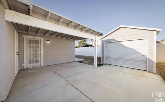 view of patio / terrace with a garage, an outbuilding, concrete driveway, and fence