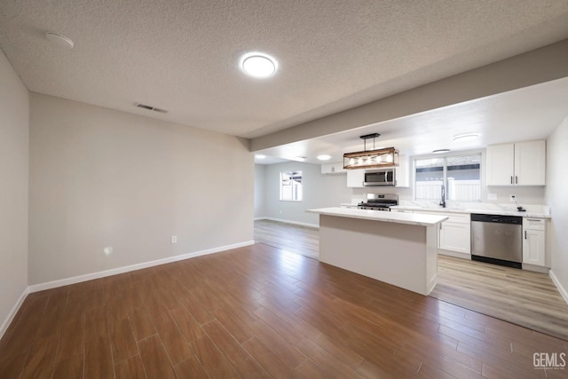 kitchen featuring light wood-style flooring, open floor plan, white cabinetry, stainless steel appliances, and light countertops