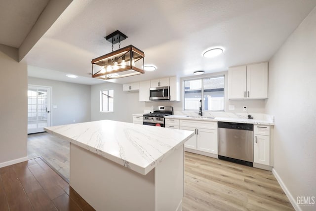 kitchen featuring light wood finished floors, light stone countertops, stainless steel appliances, white cabinetry, and a sink