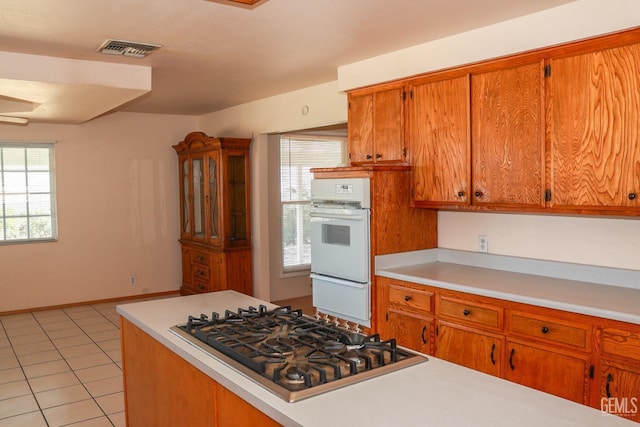 kitchen featuring light tile patterned floors, light countertops, visible vents, stainless steel gas stovetop, and brown cabinetry