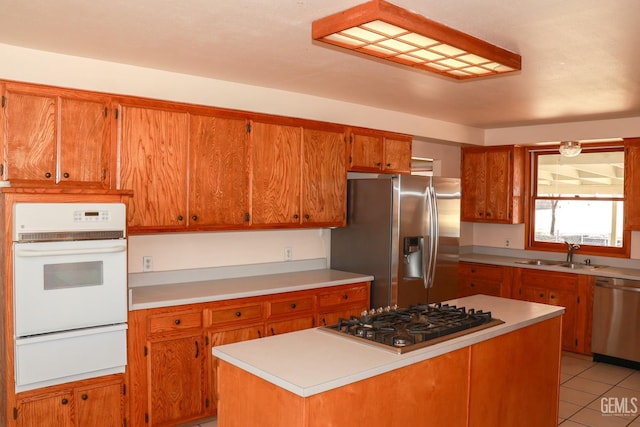 kitchen with brown cabinetry, appliances with stainless steel finishes, light countertops, a sink, and a warming drawer