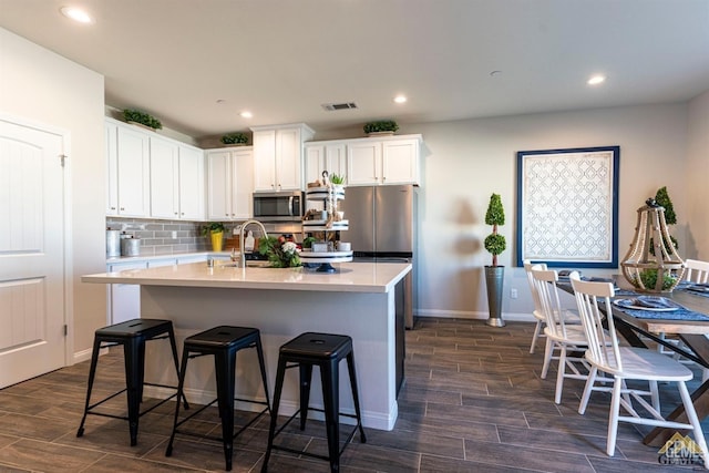 kitchen featuring white cabinets, a center island with sink, a kitchen bar, and stainless steel appliances