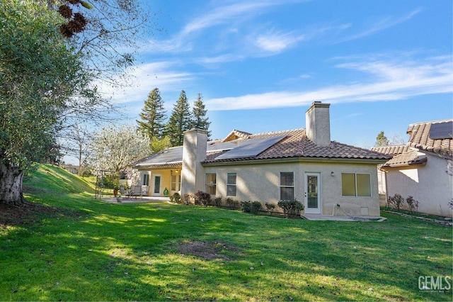 back of house featuring a tile roof, a yard, a patio, stucco siding, and solar panels