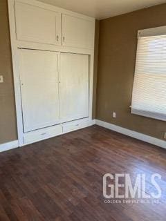 unfurnished bedroom with a closet, baseboards, and dark wood finished floors