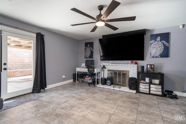 living room featuring baseboards, a brick fireplace, and ceiling fan